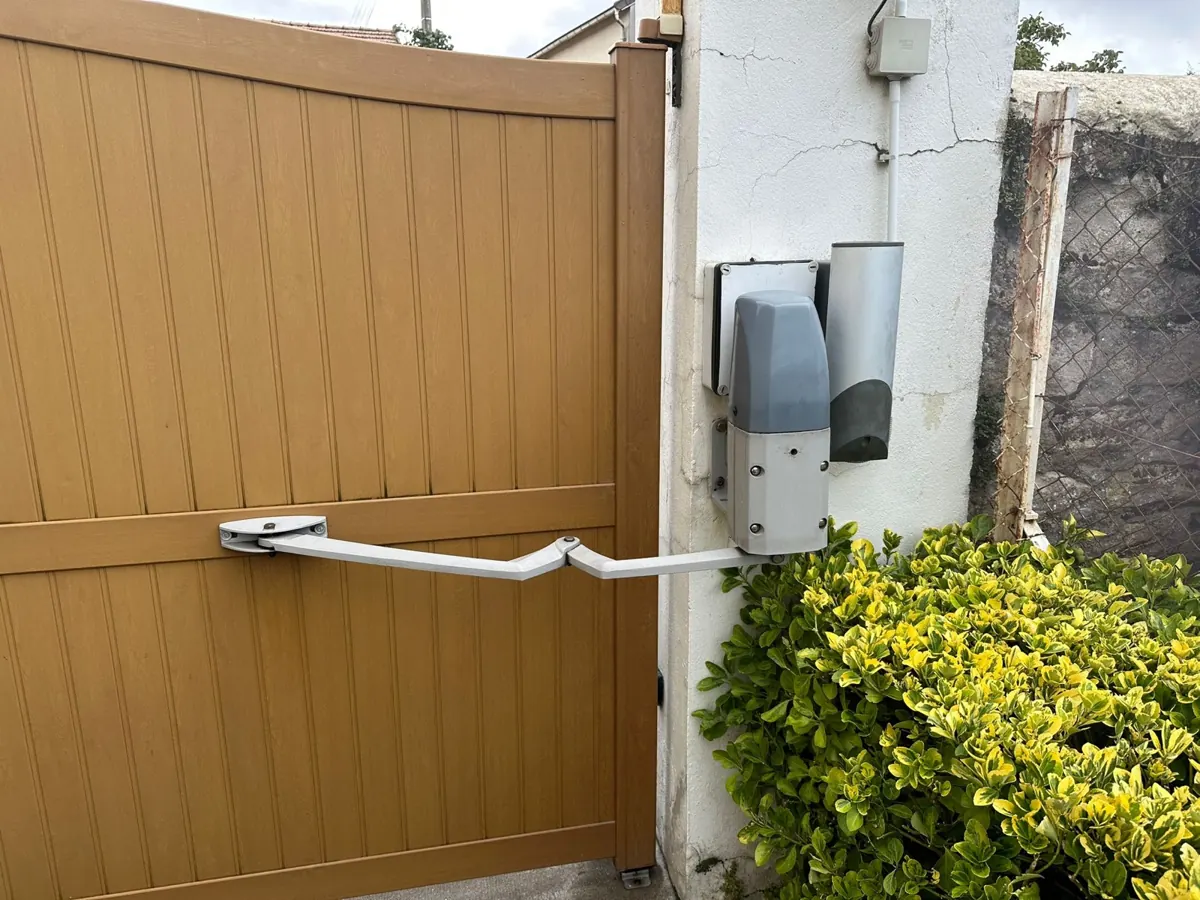 Bras articulé et moteur fixés au pilier d'un portail battant en PVC, après remplacement