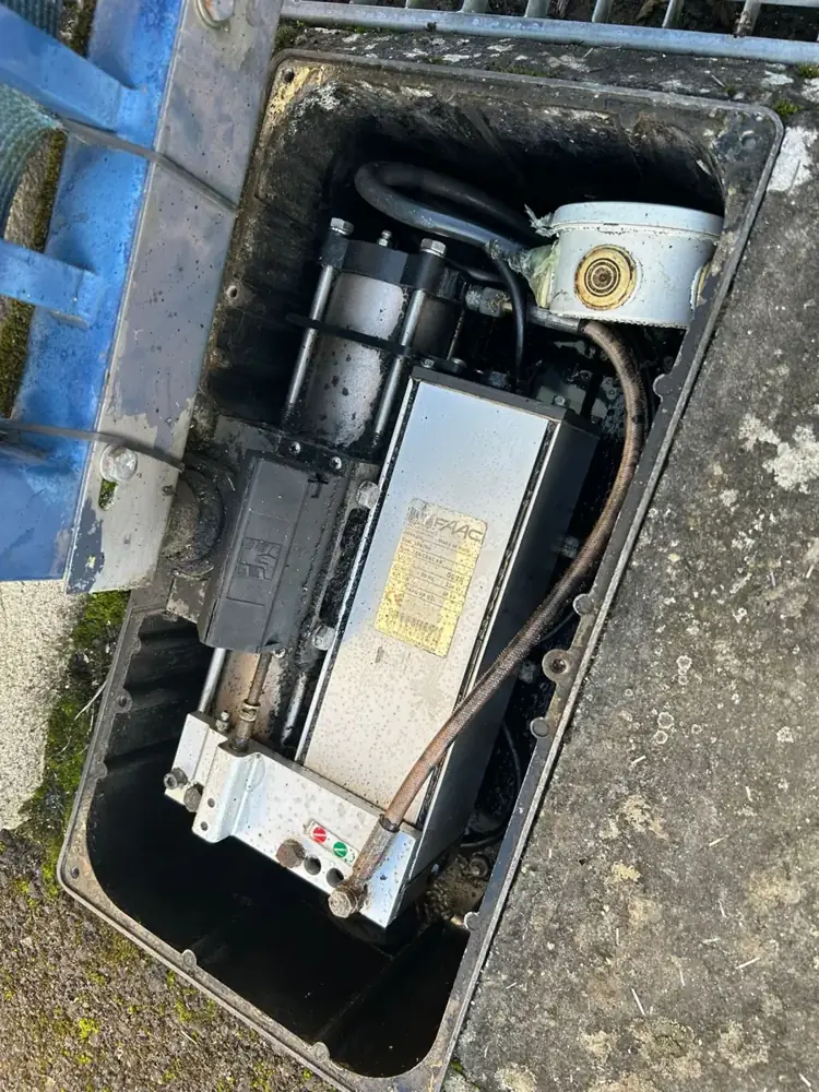 Moteur enterré dans son caisson au pied du vantail, trappe ouverte pendant l'intervention