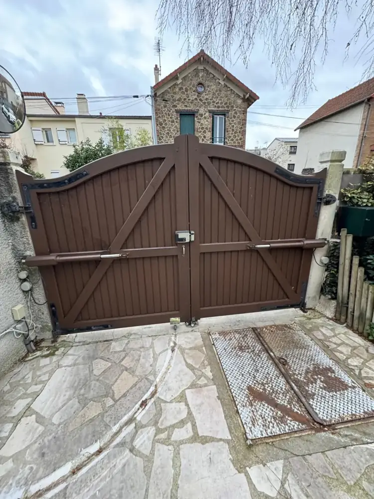 Portail battant en bois motorisé par deux vérins, devant une maison en meulière d'Île-de-France