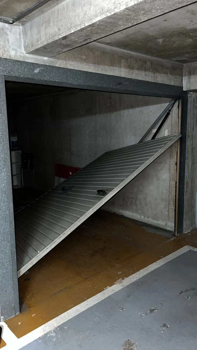 Porte basculante de box entrouverte dans un parking de copropriété
