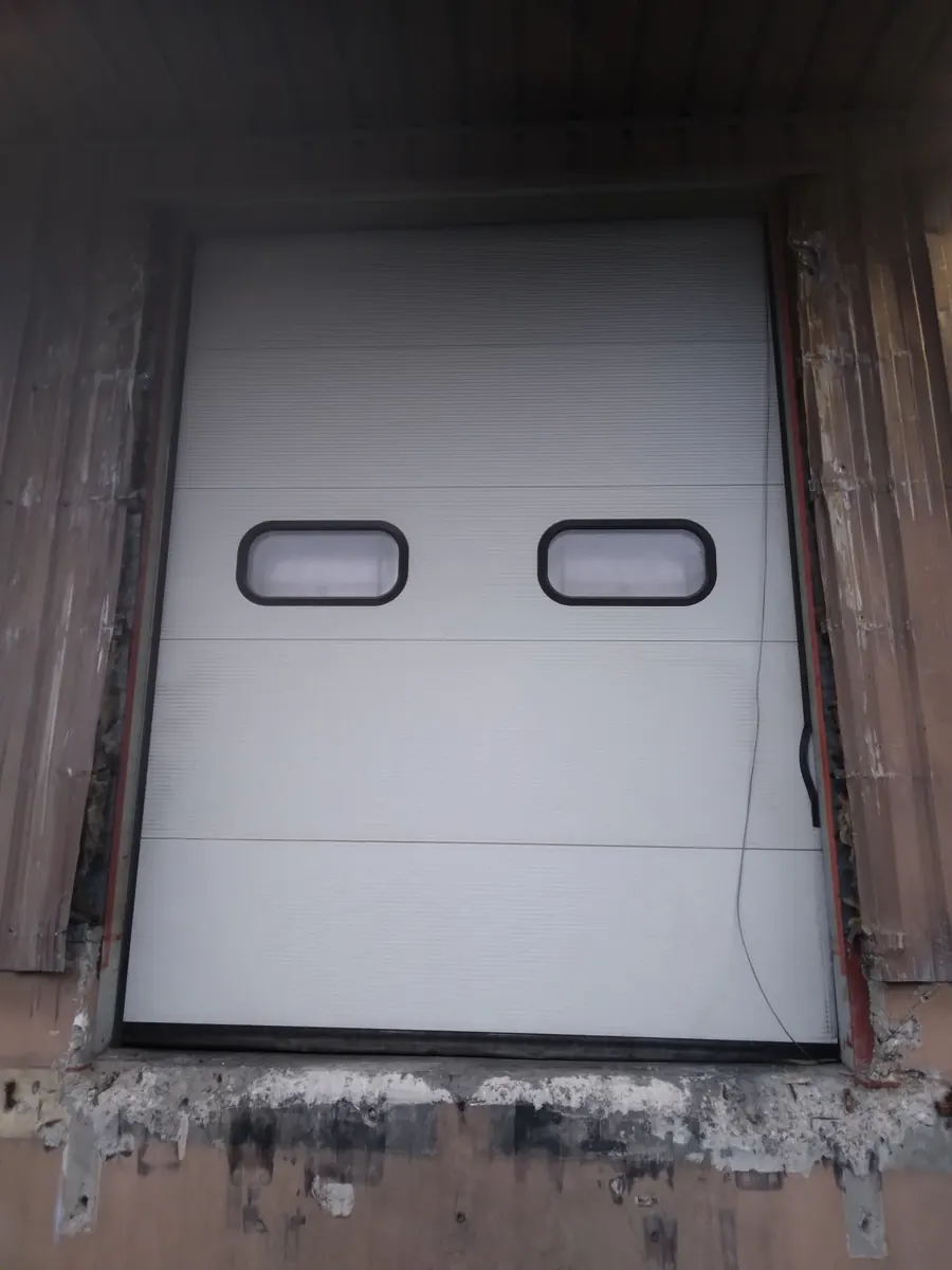 Porte sectionnelle industrielle blanche à hublots sur un quai de chargement