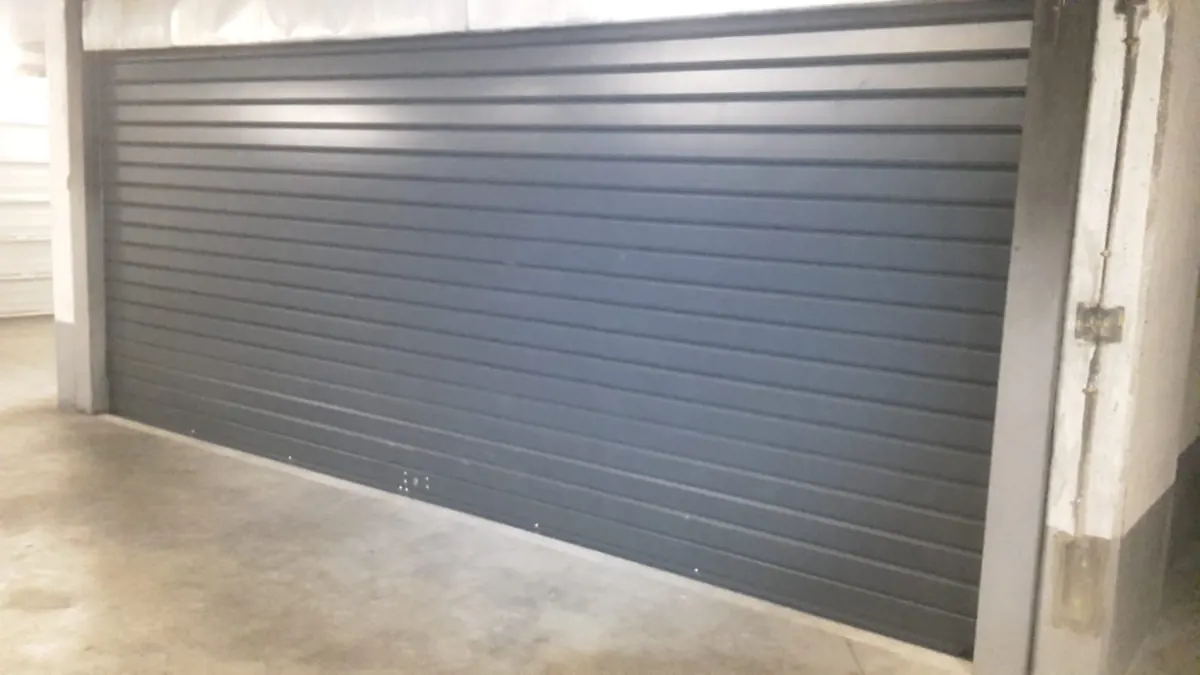 Rideau métallique gris d'un accès de parking en sous-sol, remis en service